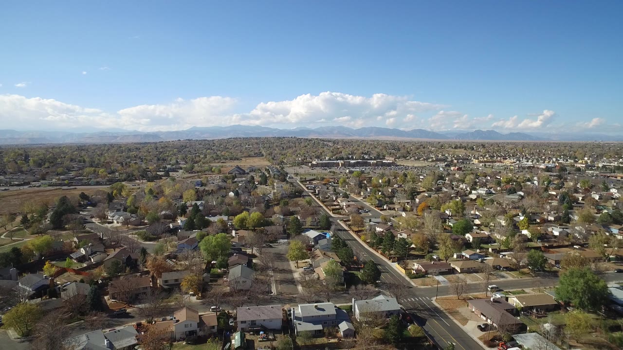 Aerial view of a suburban neighborhood with roads, houses, trees, and distant mountains.