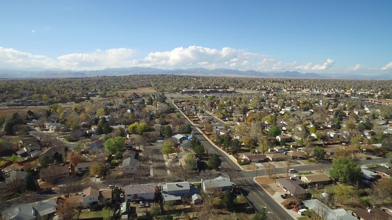 Mid-clip aerial frame of Hidden Lake, Colorado, showing detached homes and straight roads across the foreground with a broad sky and no visible people.