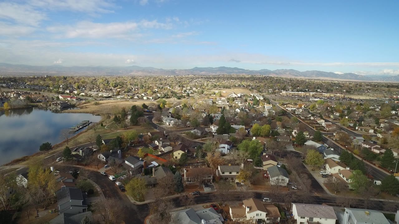 Opening aerial frame over Hidden Lake, Colorado, with calm water at left, houses and trees below, distant mountains on the horizon, and no visible people.