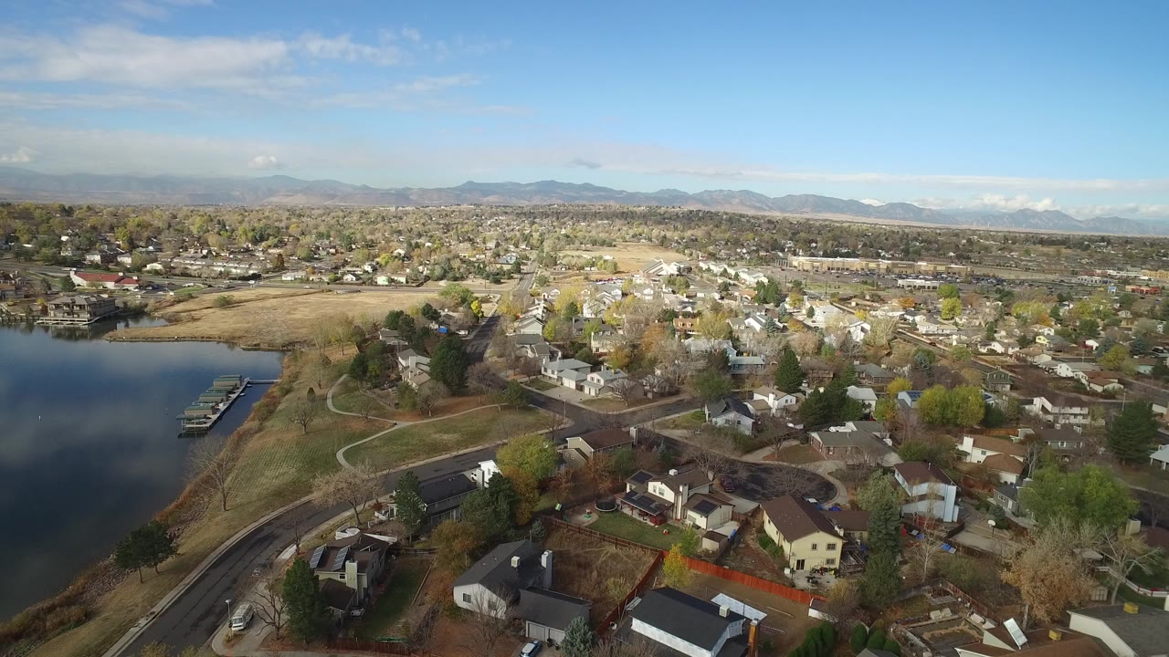 Aerial view of lake shoreline, docks, houses, roads, trees, and distant mountains.