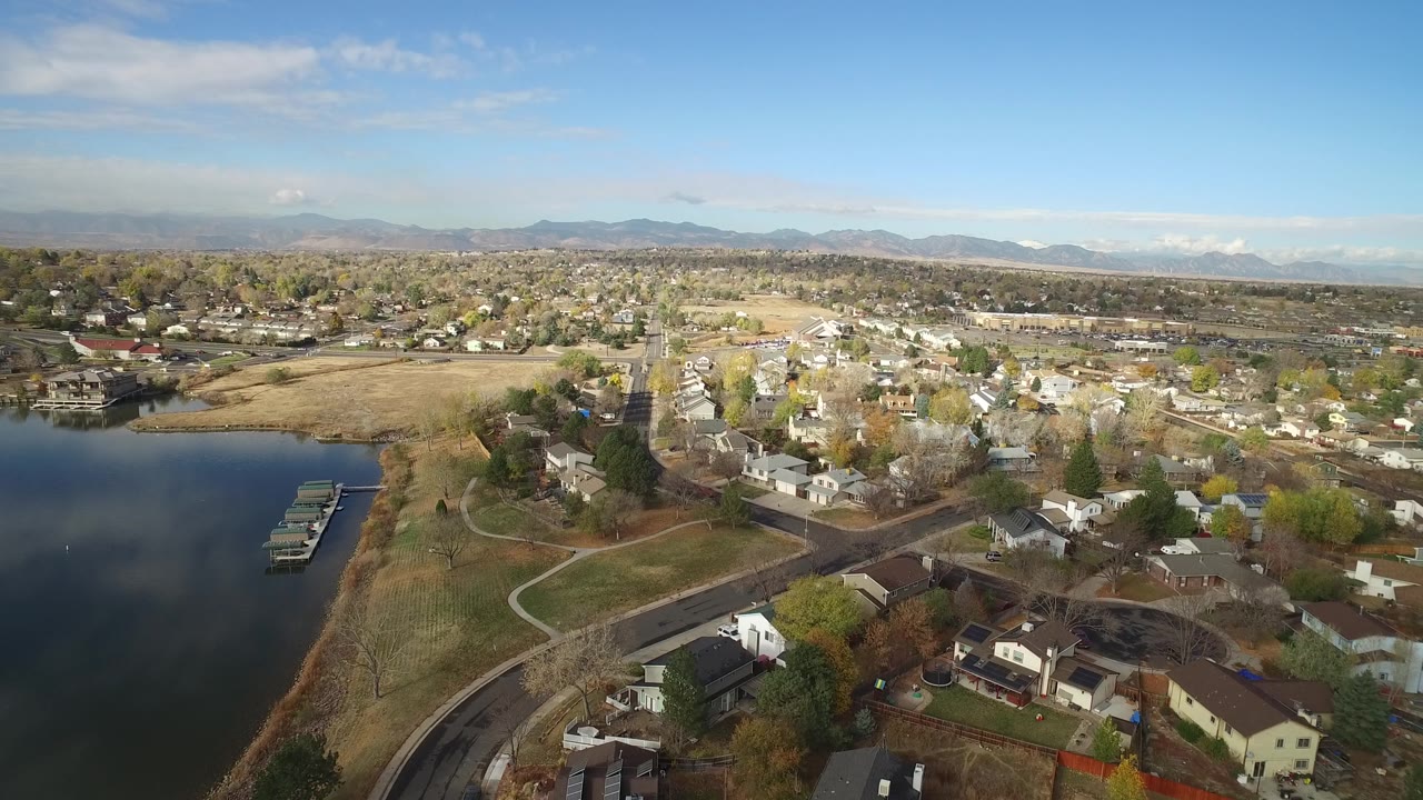Wide aerial view of a lakefront residential district with open tan fields and houses.