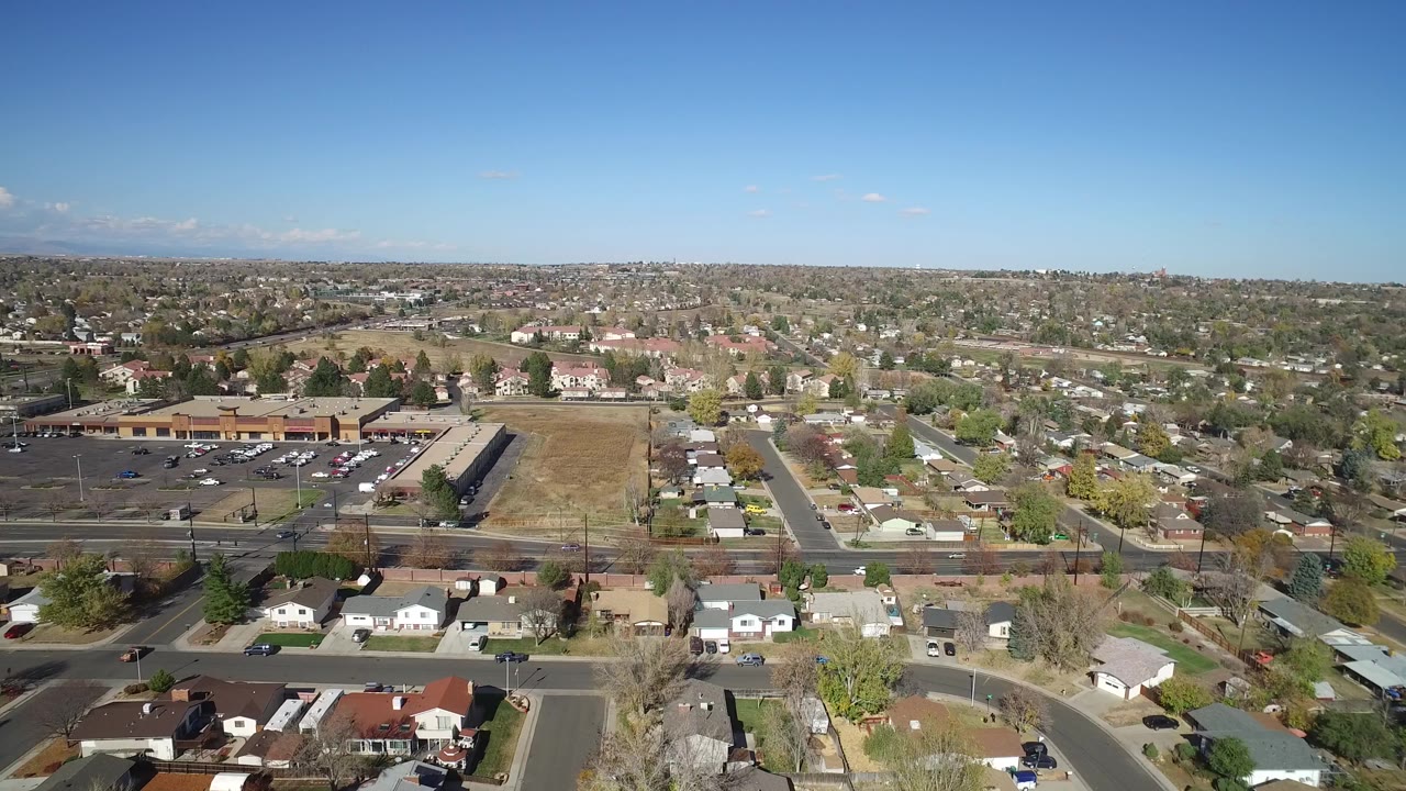 Aerial view of suburban homes, roads, parking lot, and blue sky.