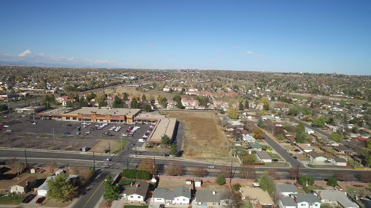 Aerial view over suburban roads, parking lots, homes, and distant mountains.