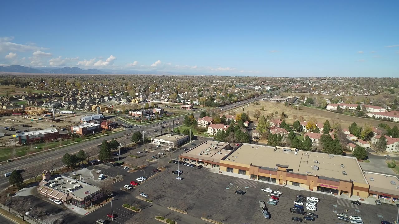 Aerial view over commercial rooftops, roads, homes, fields, and distant mountains.