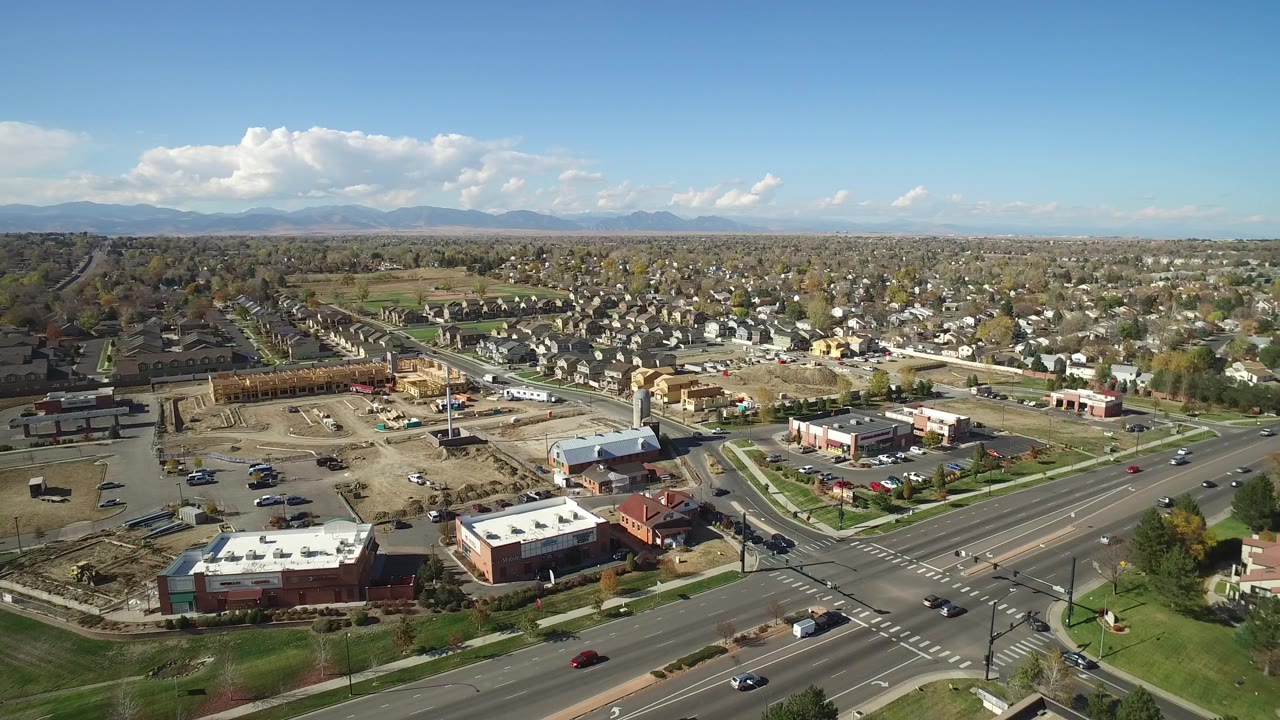 Aerial view of a suburban intersection, shops, houses, and distant mountains.