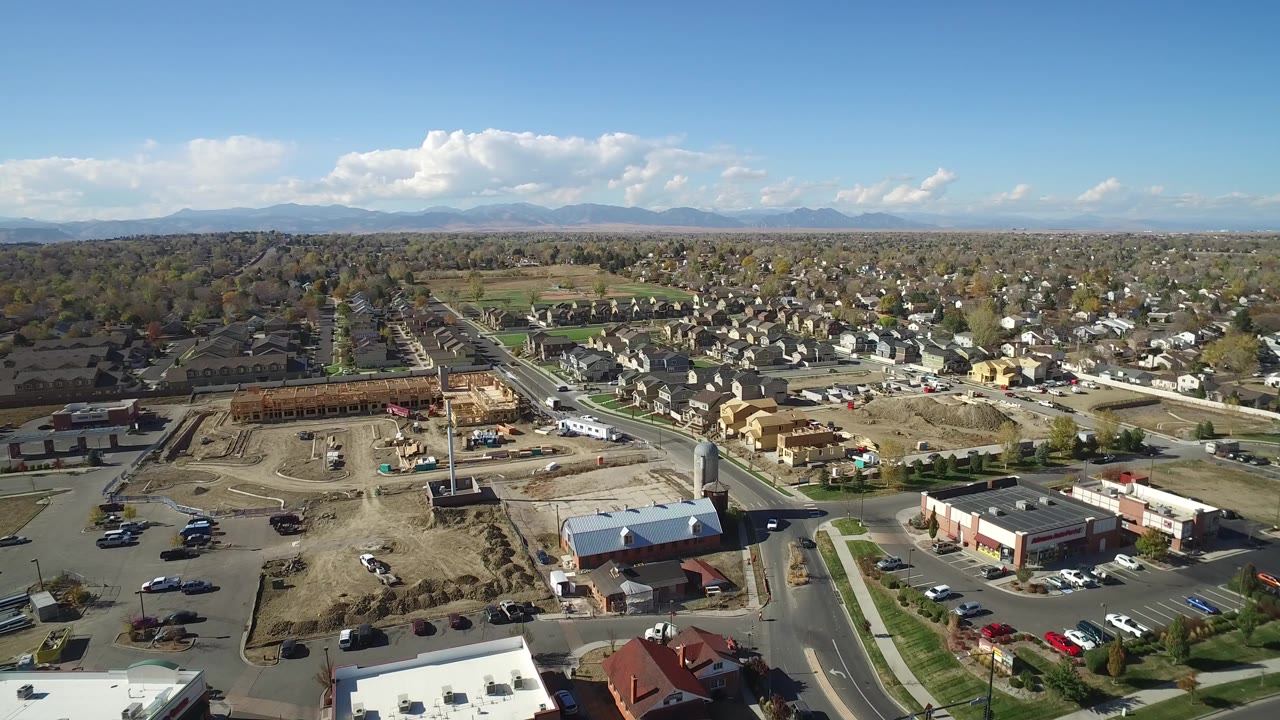 Aerial view over suburban roads, construction ground, homes, and distant mountains.