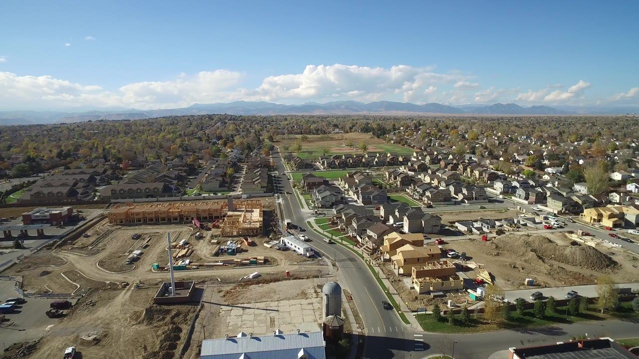 Wide aerial view of a residential area with construction sites and distant mountains.