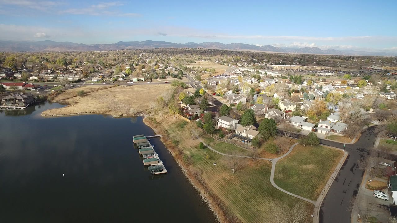 Aerial view of lake, dock slips, shoreline paths, homes, and distant mountains.