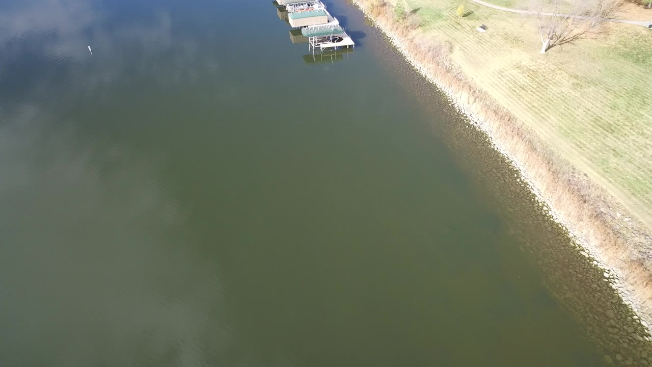 Aerial frame over Hidden Lake, Colorado, showing green water, a diagonal grass shoreline, covered docks near the top edge, and no visible people.