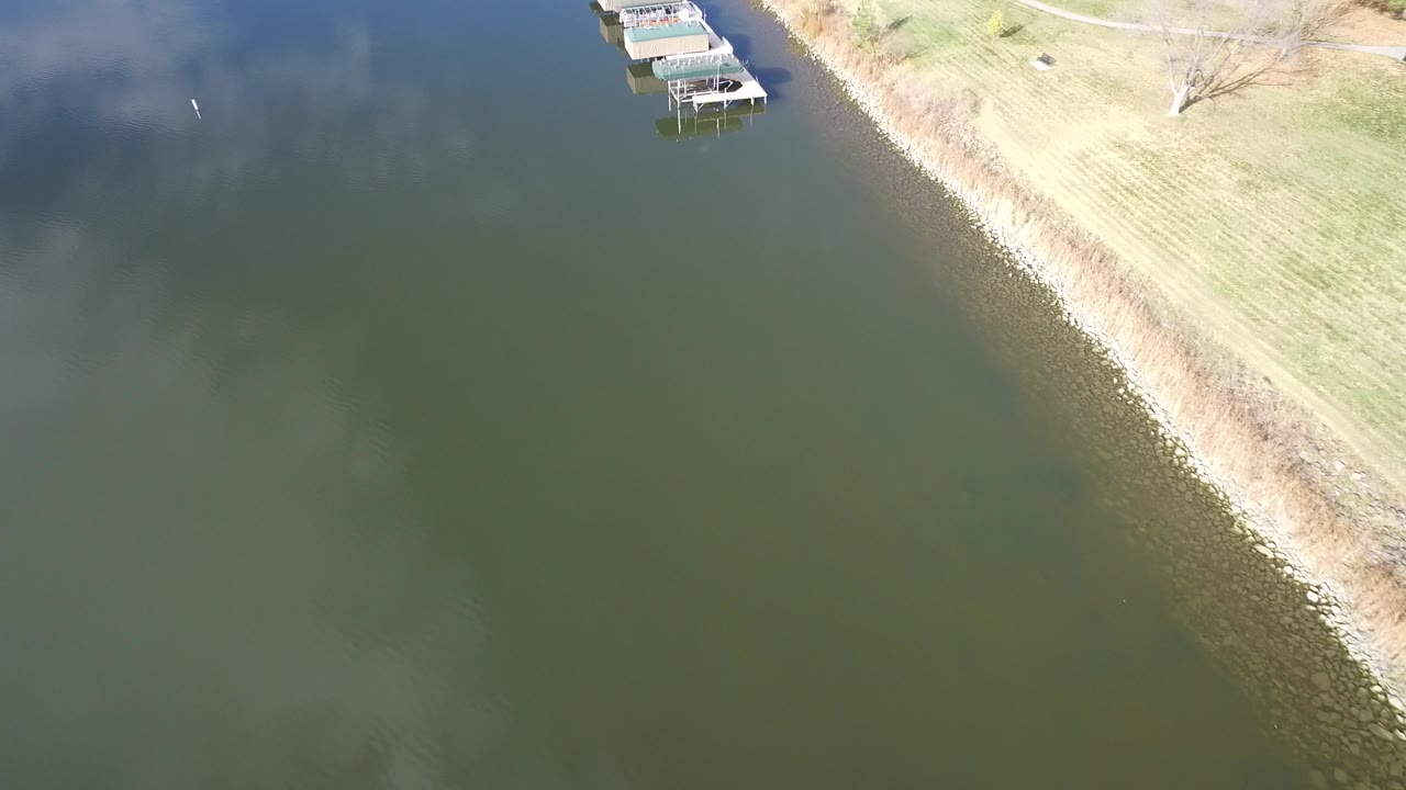 Aerial view at 0:01 over Hidden Lake, Colorado, with the shoreline tighter to the right side, covered docks near the top, open green water, and no visible people.