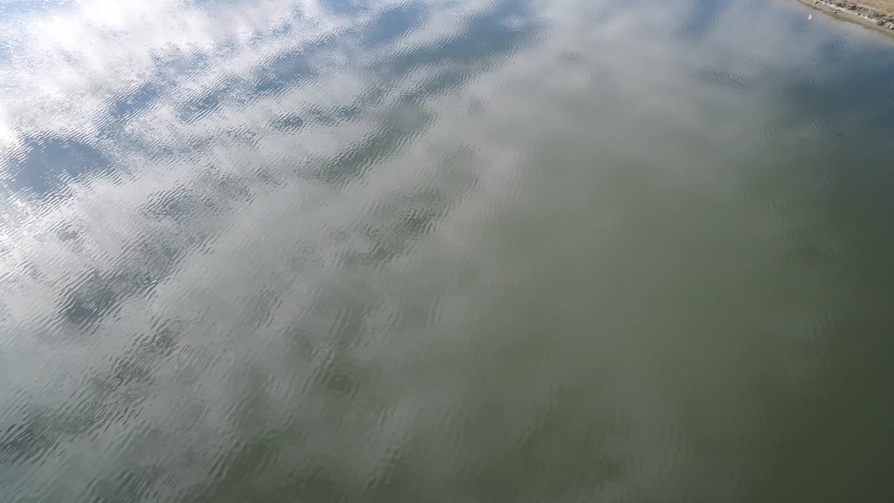 Overhead view of Hidden Lake, Colorado water with soft ripples, white cloud reflection across the upper left, blue sky reflection near the top, and no visible people.
