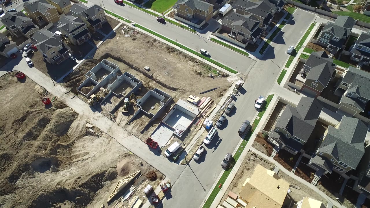 High overhead view in Hidden Lake, Colorado showing finished houses, paved streets, parked vehicles, dirt lots, and concrete home foundations with no visible people.