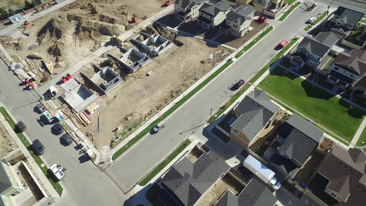 High aerial view over Hidden Lake, Colorado, showing paved neighborhood roads, finished homes, dirt construction lots, parked vehicles, green lawns, and no visible people at the start of the clip.