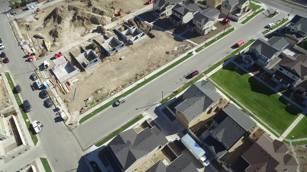 Aerial view of an intersection with homes, parked vehicles, and active building lots.