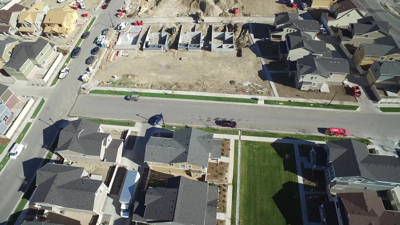 Drone-like overhead frame in Hidden Lake, Colorado with a central residential road, parked cars, newly built houses, graded dirt lots, and no visible people.
