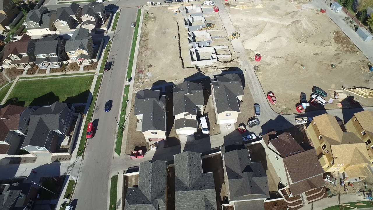 Aerial view of suburban homes, a paved street, lawns, and construction lots.