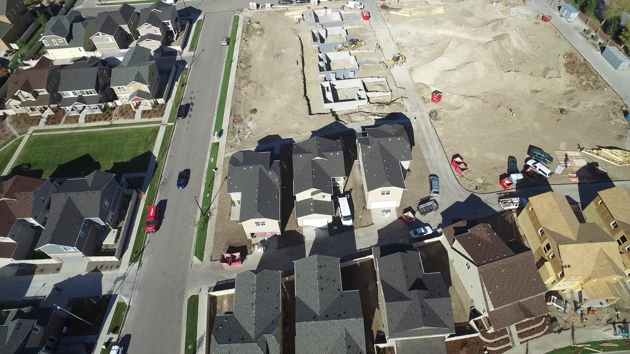 Aerial frame over Hidden Lake, Colorado with dark rooflines, a broad pale dirt lot, several parked vehicles, and partly built houses near the center of the view.