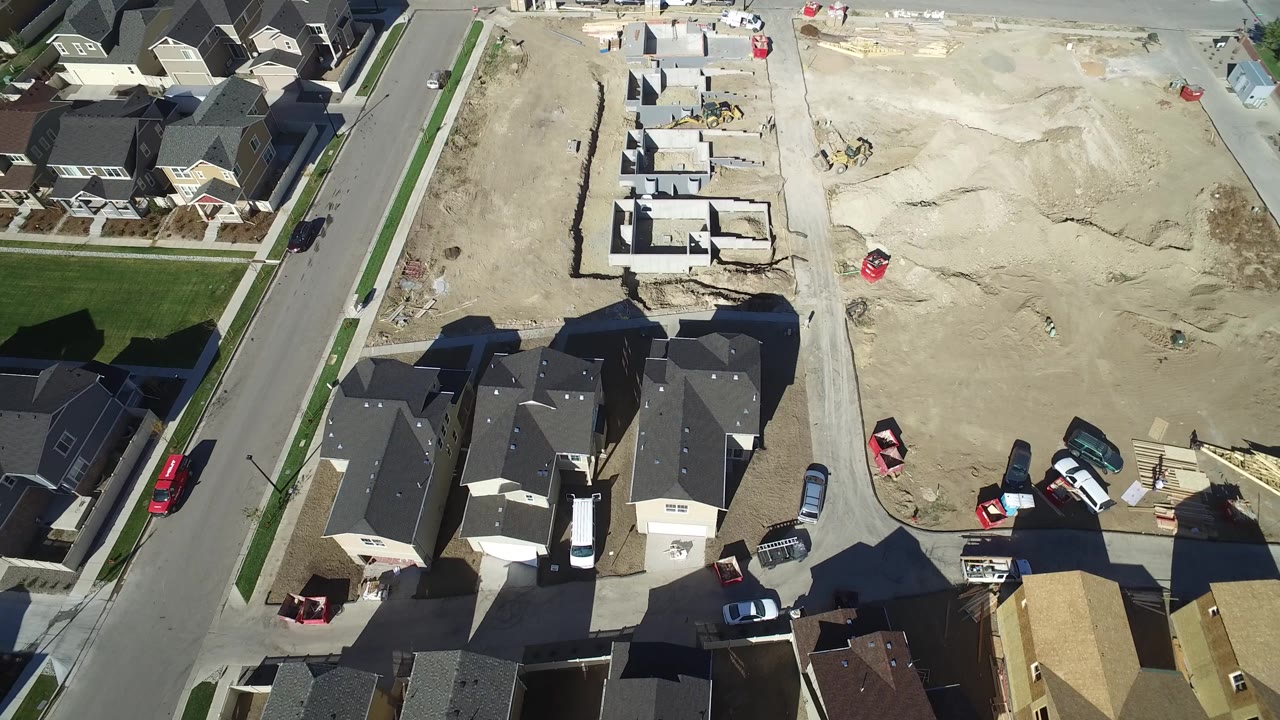 A slightly shifted aerial view in Hidden Lake, Colorado shows foundation walls, scraped dirt, nearby roofs, driveways, parked vehicles, and no visible people.