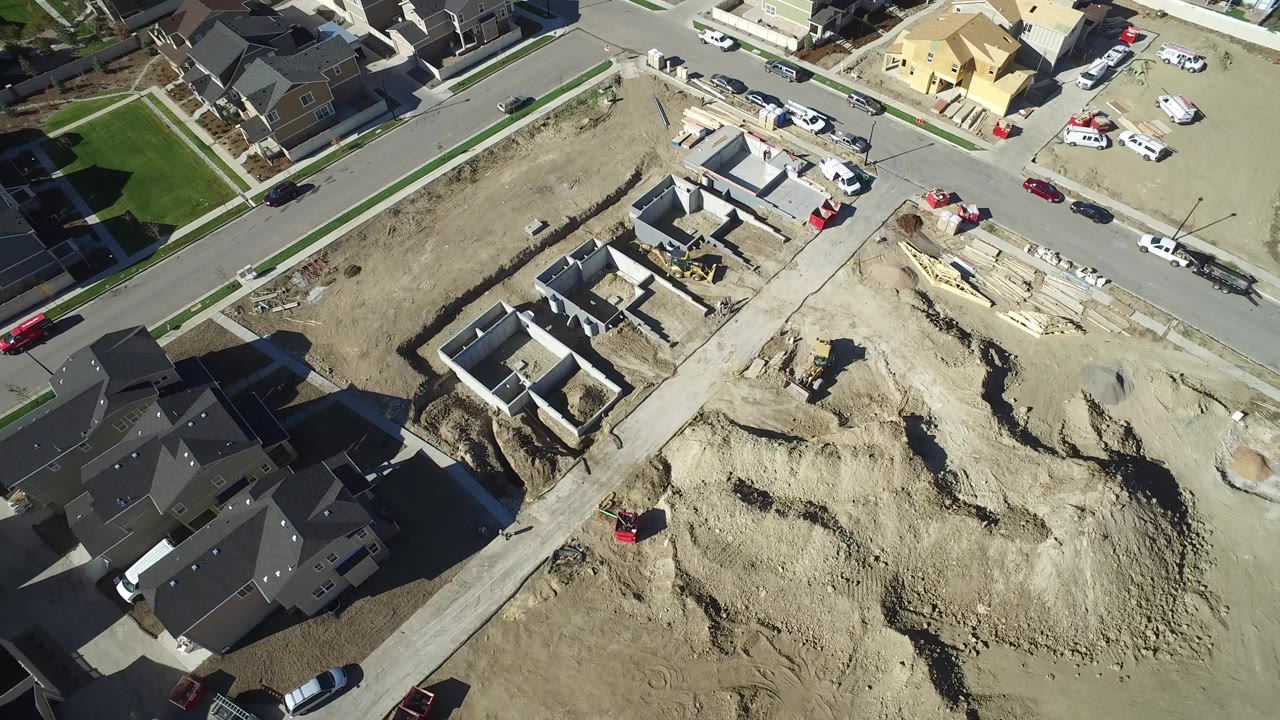 Aerial view of dirt mounds, house foundations, roads, cars, and nearby homes