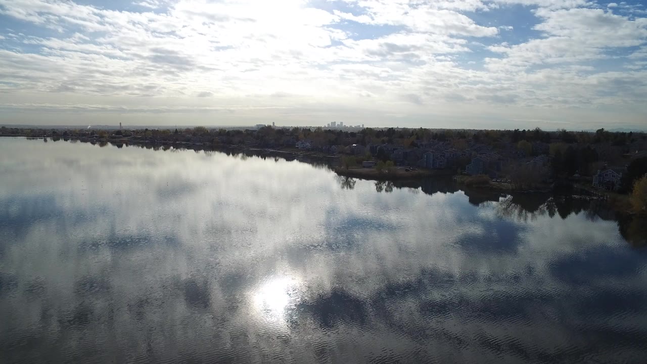 Aerial view of a large lake reflecting clouds and sun glare.