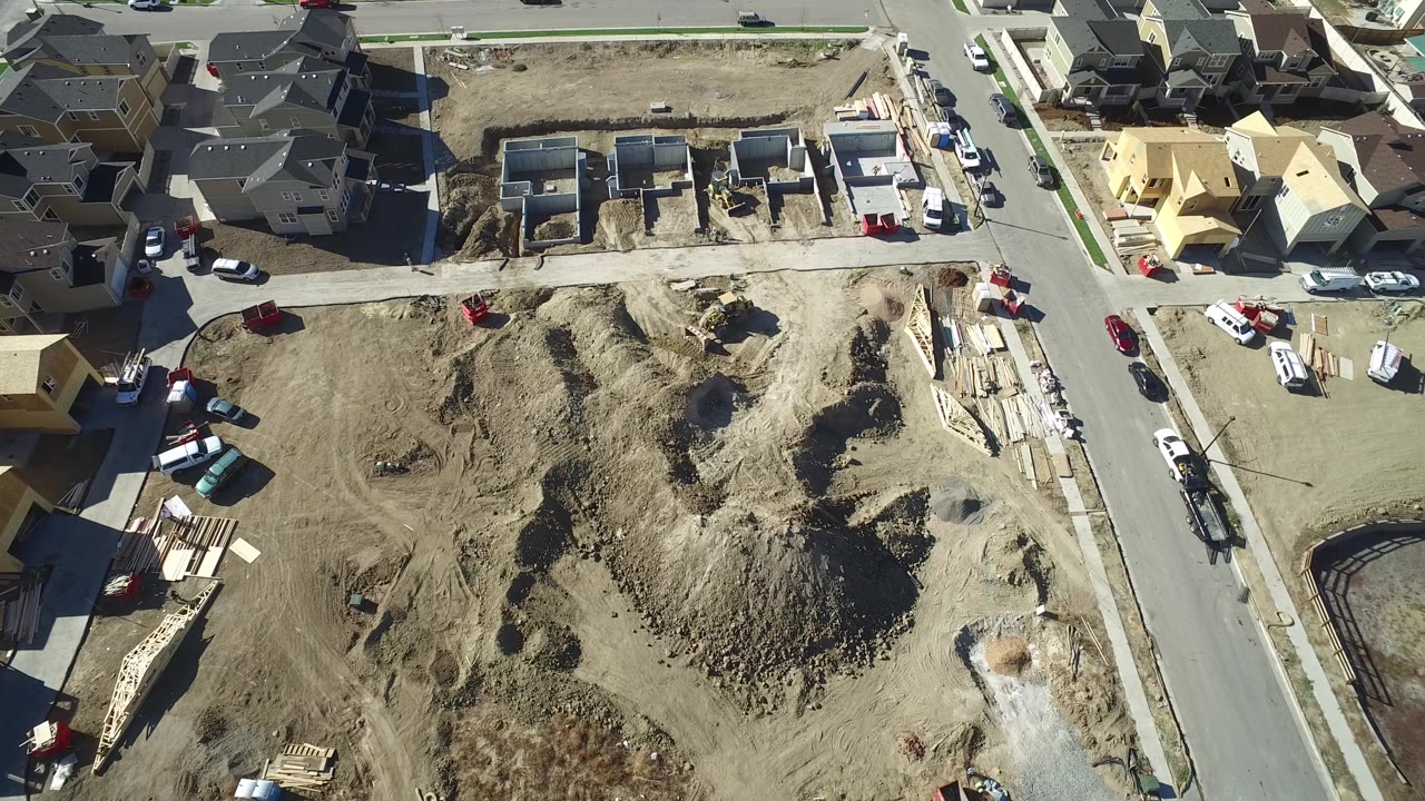 Aerial view of unfinished houses and a large dirt lot in a suburban block.