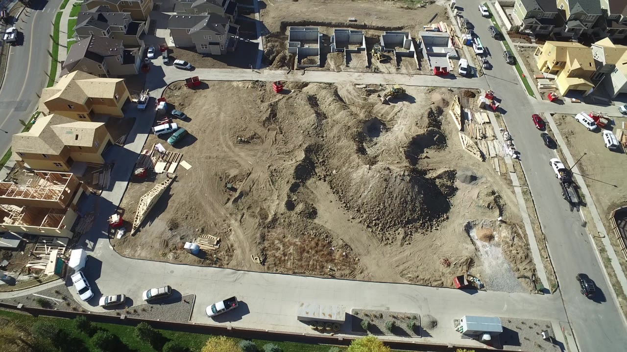 Aerial view of a dirt construction lot beside roads and houses.