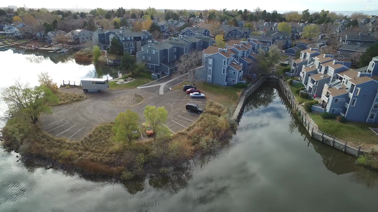 A slightly shifted aerial view of Hidden Lake, Colorado with reflective lake water, gray residential buildings, parked cars, a small paved lot, and no visible people.