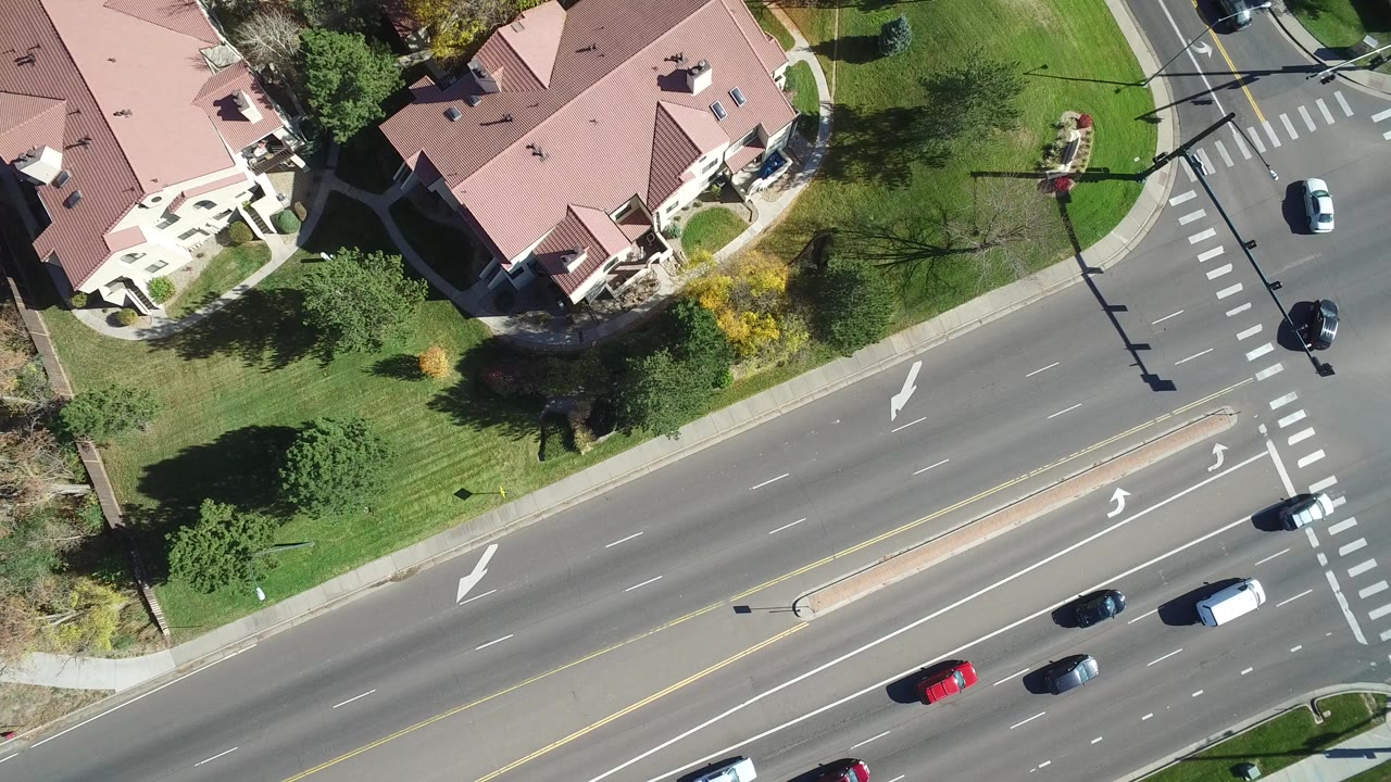 Top-down view of pink-roofed homes beside a multi-lane road and lawns.