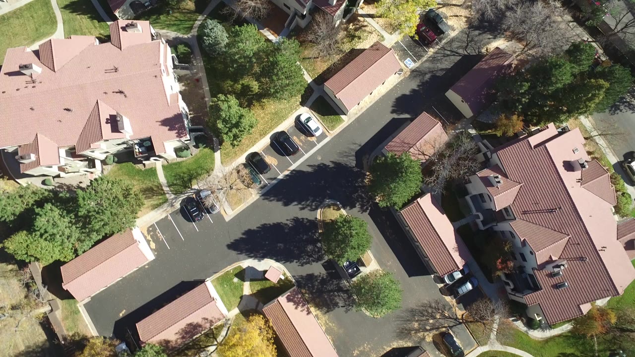 Overhead view of suburban homes, road, lawns, trees, and parked cars.