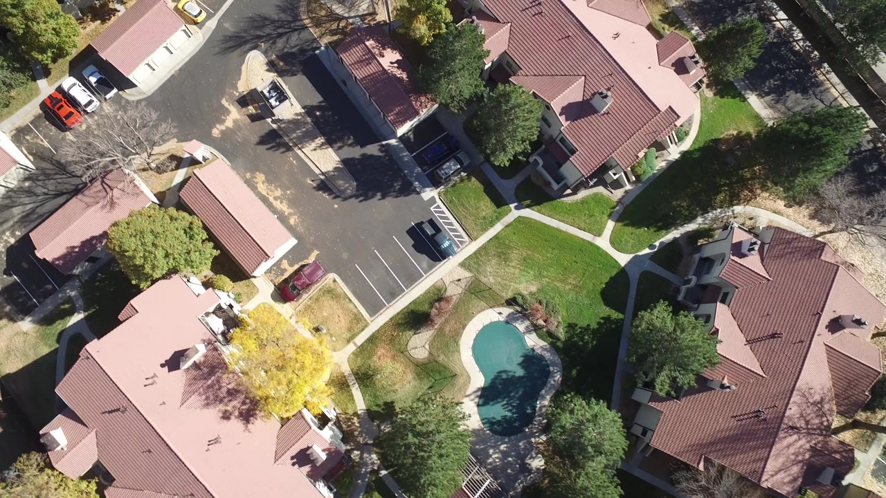 Overhead view of red-roofed homes, streets, parked cars, trees, lawns, and a small pool.