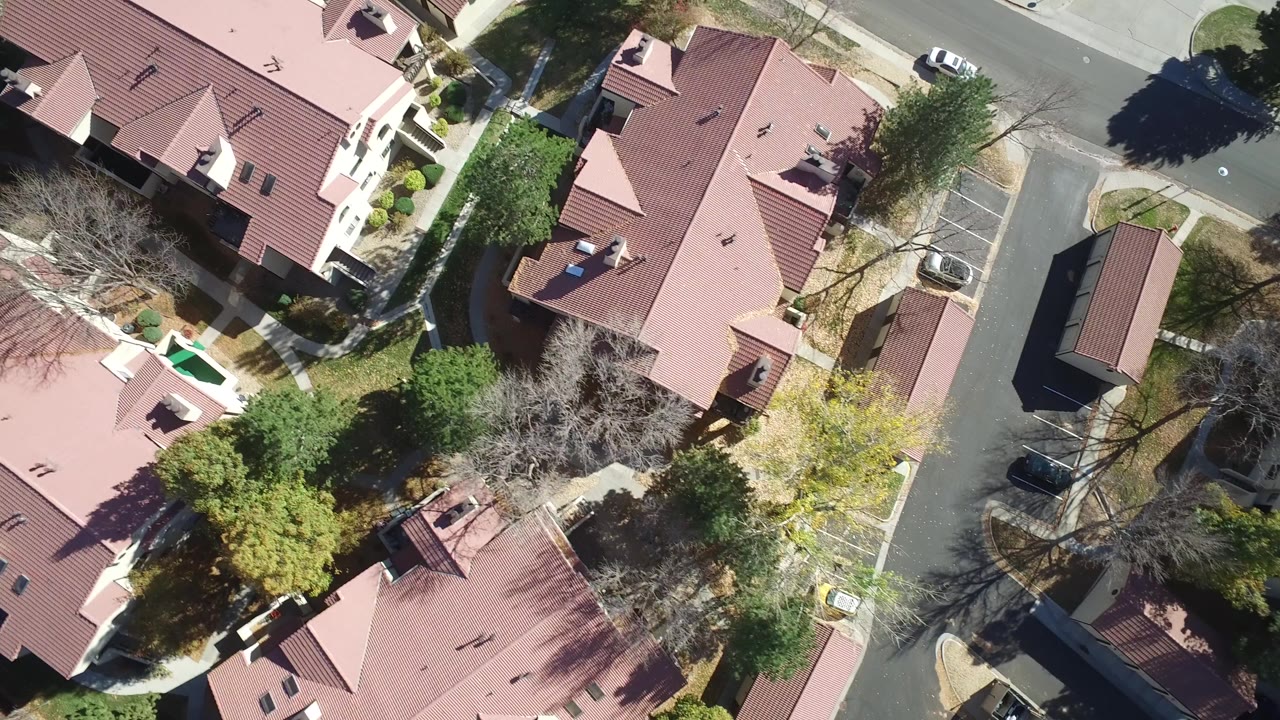 Overhead aerial frame in Hidden Lake, Colorado showing red-roofed homes, a small parking area, trees, sidewalks, and no visible people.