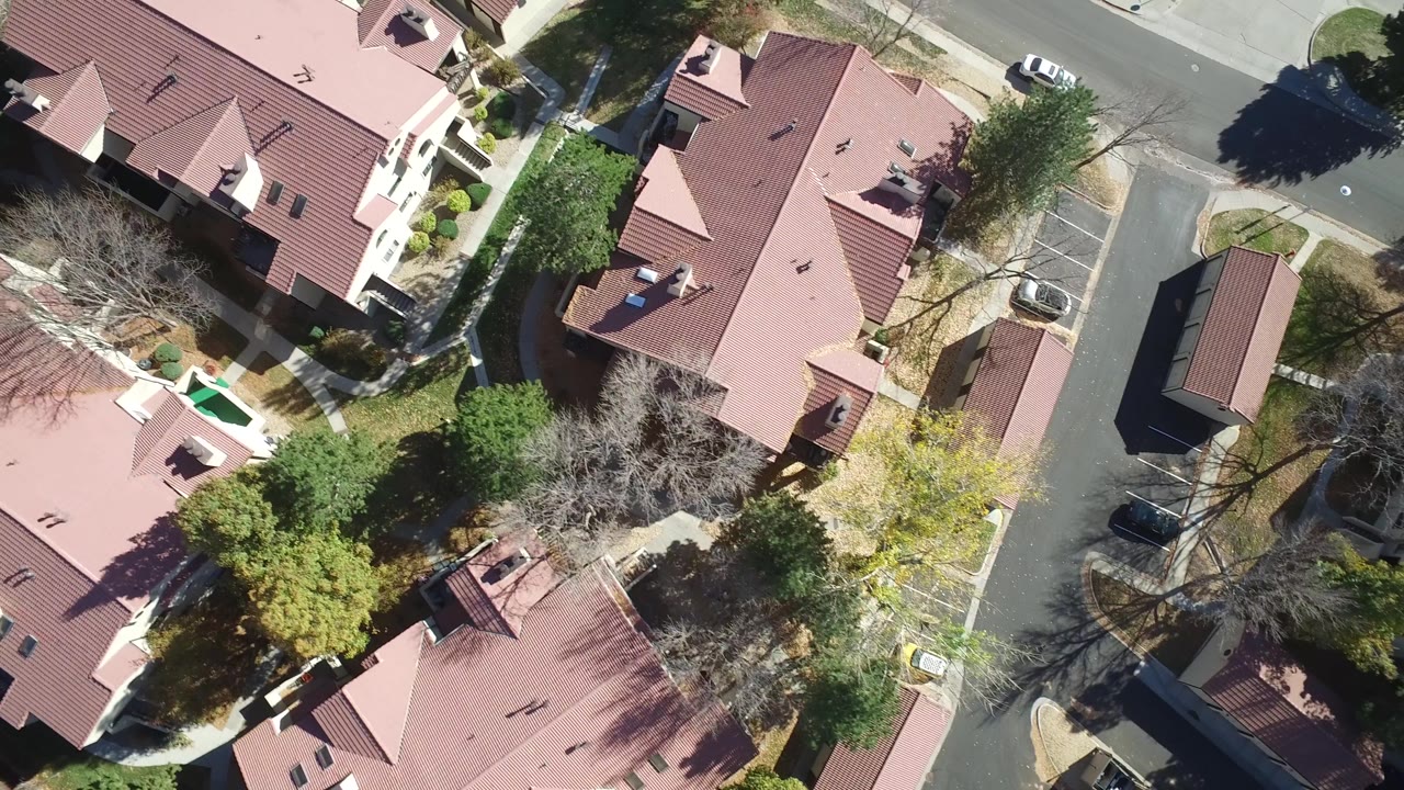 High overhead view in Hidden Lake, Colorado with red roofs filling the frame, trees casting shadows, a residential road, and no visible people.