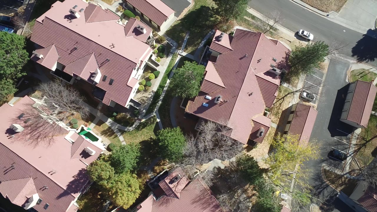 Top-down residential block with red roofs, trees, and road edges.