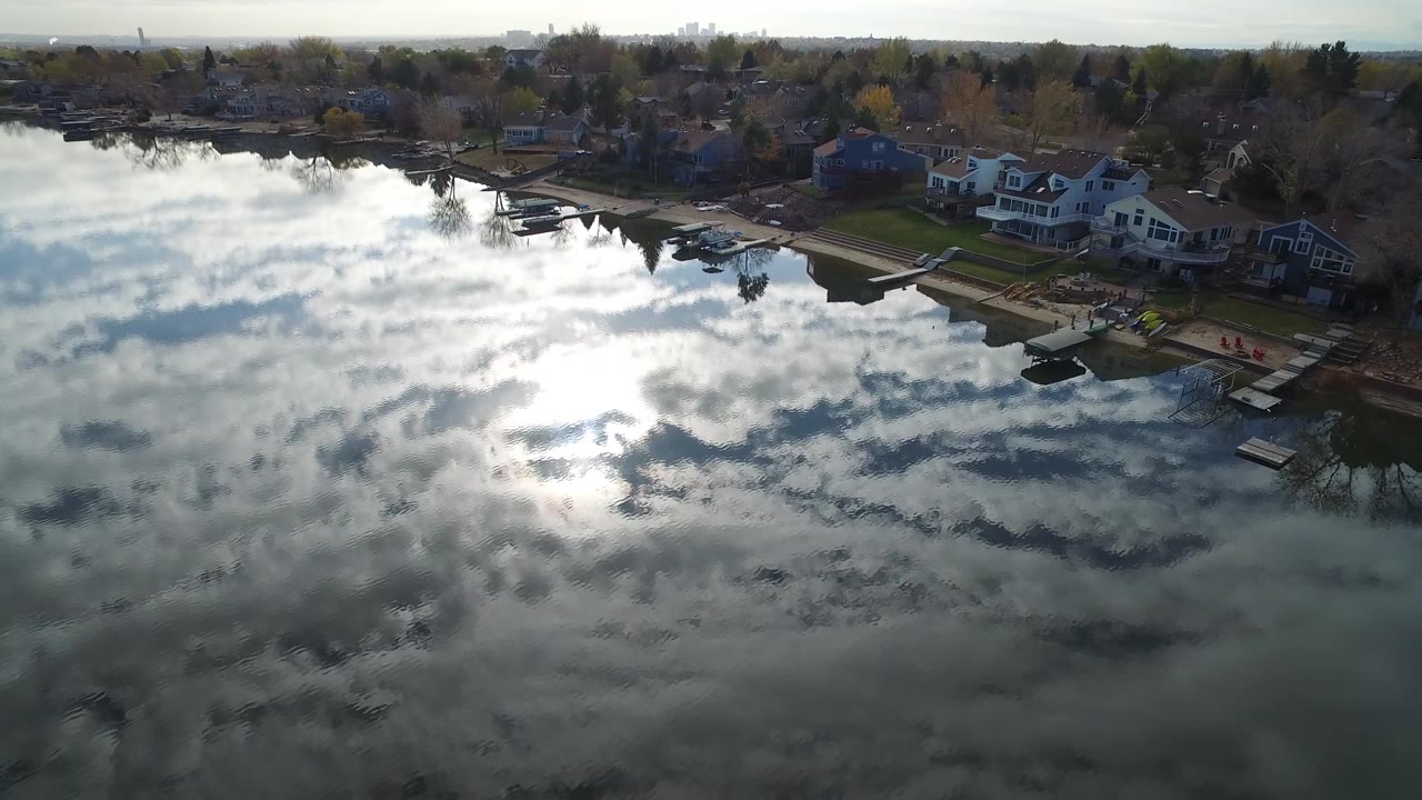Aerial view of reflective lake water beside lakefront homes and docks.
