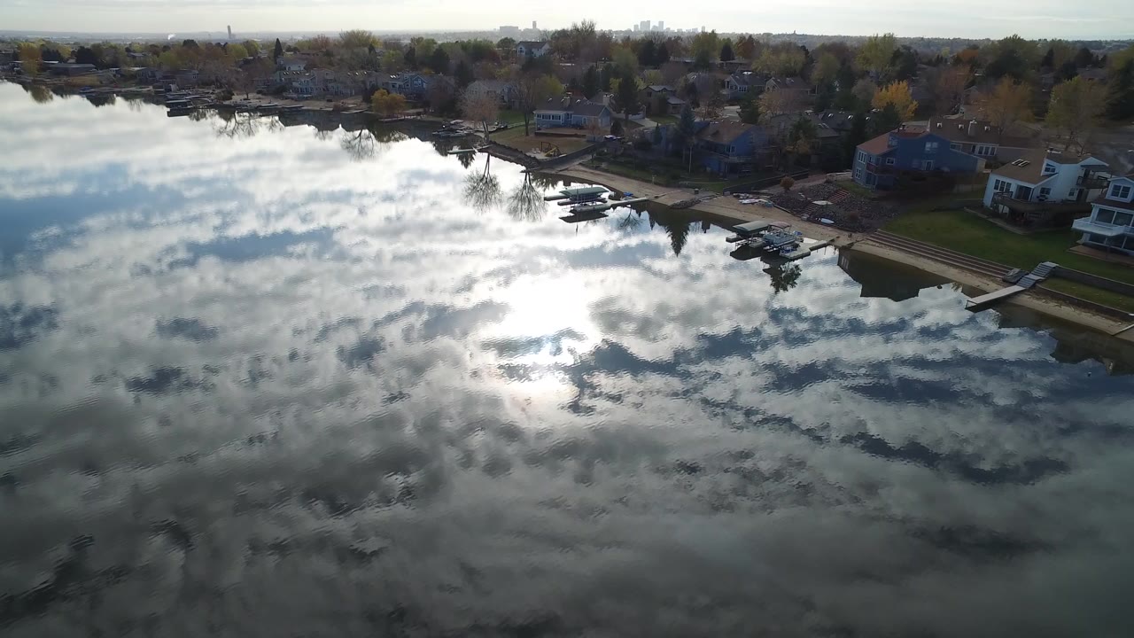 Aerial frame over Hidden Lake, Colorado with cloud reflections across dark water, docks and shoreline homes at the top edge, and no visible people.