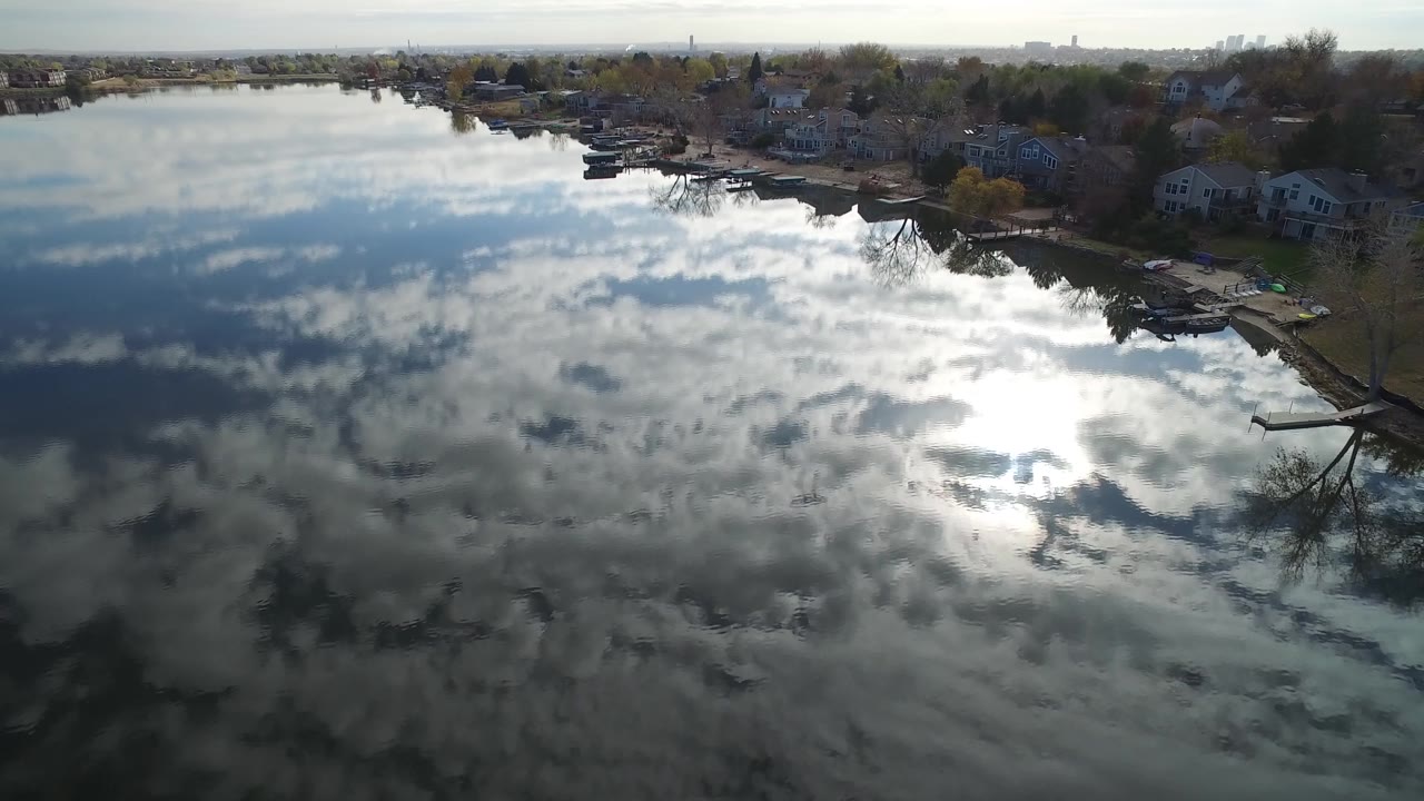 Lake shoreline with houses, docks, boats, and reflective water.