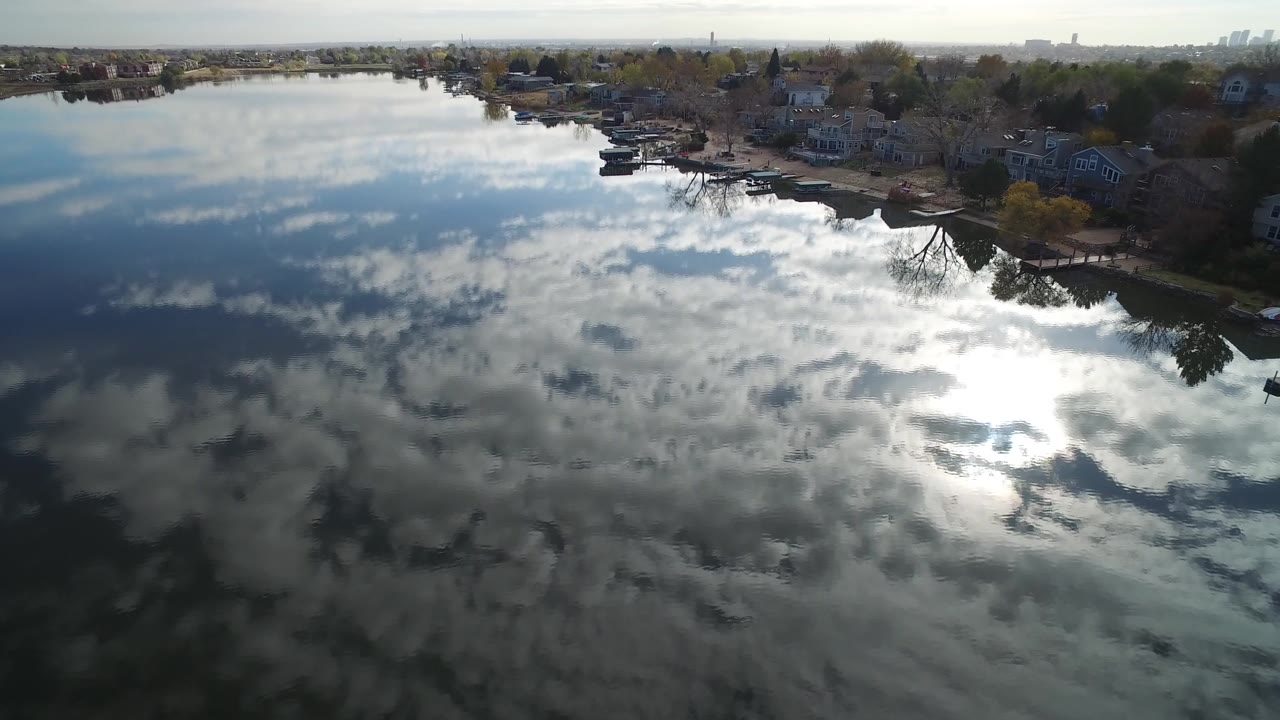 Aerial frame from Hidden Lake, Colorado showing cloud reflections on the lake, homes and docks along the far shore, and no visible people.