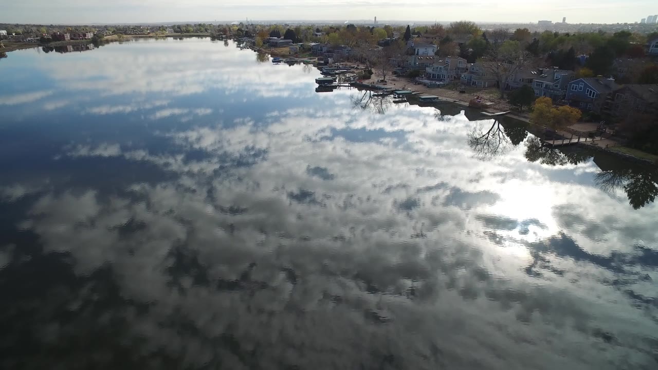 Lake reflection with a residential bank and distant buildings on the horizon.