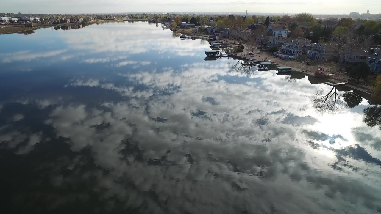 Overhead lake water reflecting clouds beside waterfront homes.