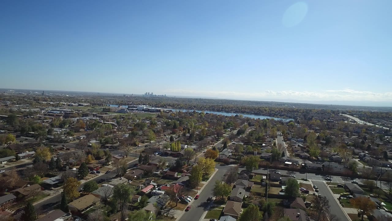 Aerial frame over Hidden Lake, Colorado showing clustered homes, straight neighborhood roads, autumn-toned trees, water beyond the houses, and no visible people.