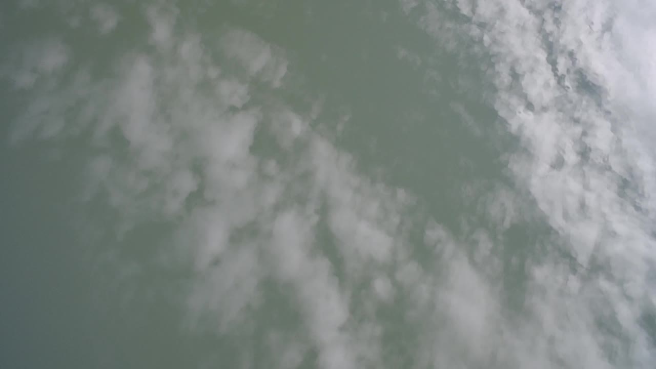 At 0:01, soft white cloud bands appear mirrored in muted lake water at Hidden Lake, Colorado, with no visible people.