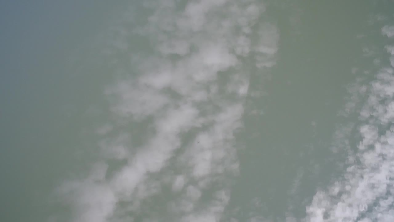 Overhead frame from Hidden Lake, Colorado showing green-gray water with a vertical band of pale white mist or cloud reflection, no visible people.