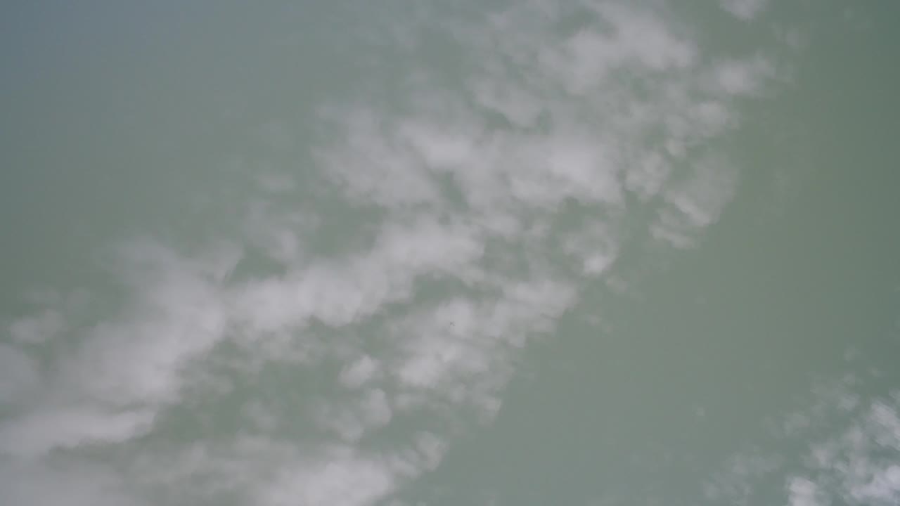Aerial-looking frame over Hidden Lake, Colorado showing blurred white cloud reflections drifting across green-gray rippled water with no visible people.