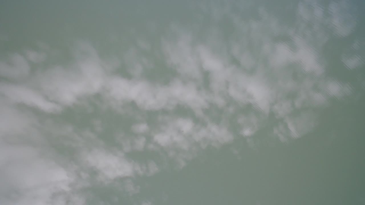 Soft white clouds over a muted blue-green aerial view.