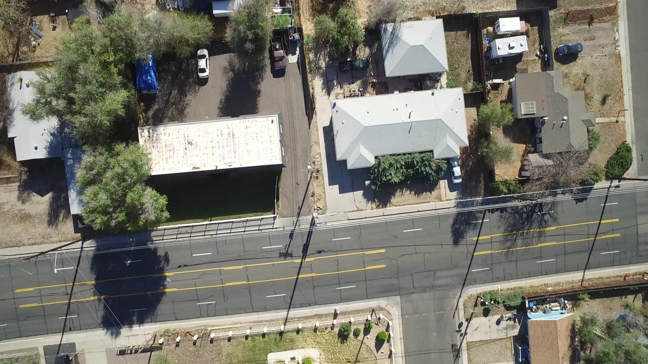 Overhead view of homes, yards, trees, parked cars, and a road.