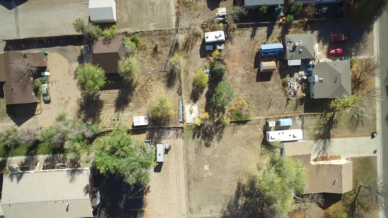 Overhead frame from Hidden Lake, Colorado showing private homes, dry yards, green trees, pale roads, trailers, and parked vehicles, with tiny possible people not clearly identifiable.