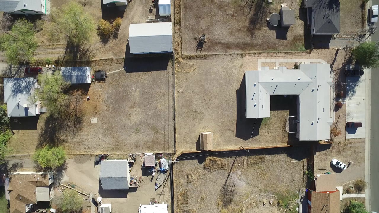 Overhead view of houses, fenced lots, trees, sheds, and parked vehicles.