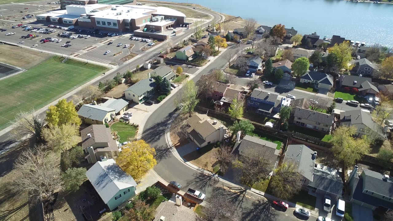 High angle view of houses, a road curve, open field, lake, and a large lakeside structure.