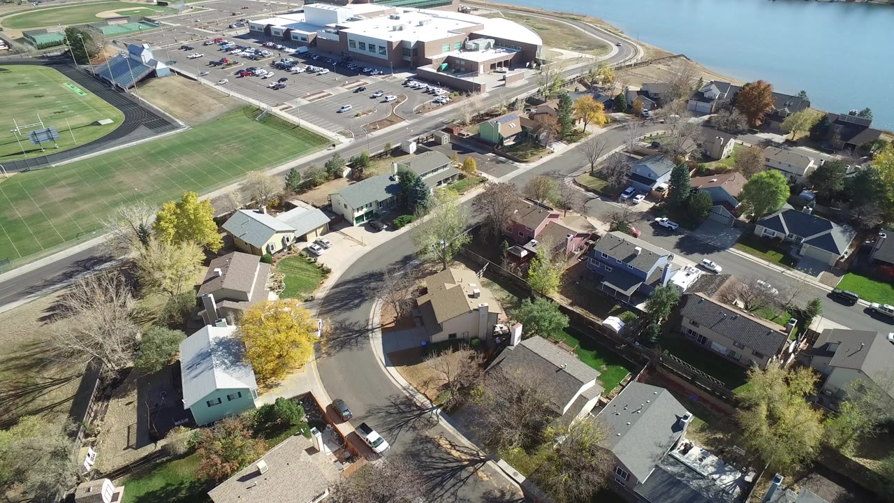 High aerial frame over Hidden Lake, Colorado with private homes in the foreground, a green football field at left, a large building by the water at top, and no visible people.