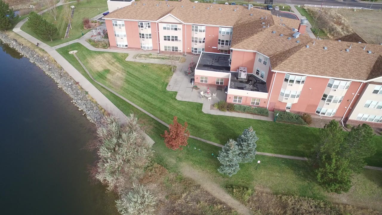 Aerial view of lakefront residential buildings, lawns, paths, and trees.